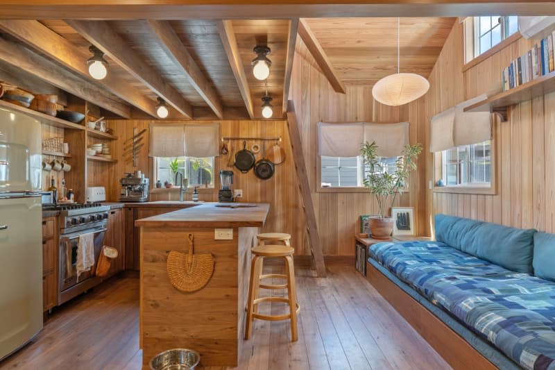 Noguchi pendant lamp hanging in living room space with long blue quilted sofa across from kitchen with vintage green refrigerator and vintage lighting with   tulip-like silhouettes hung from ceiling.