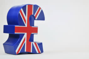 Blue plastic money box in the shape of the UK pound sterling symbol, with the Union Jack flag on the front. Studio shot against