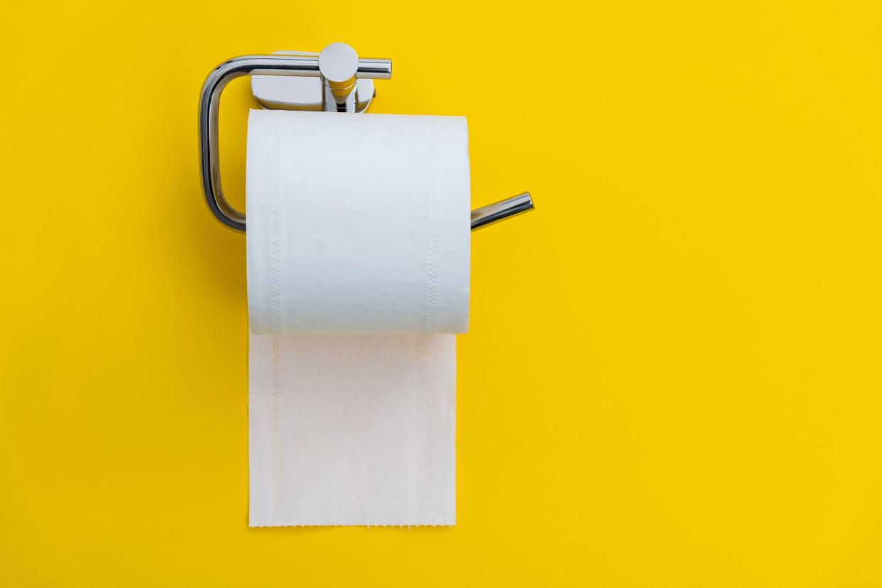 Roll of toilet paper hanging on a toilet paper holder on a bright yellow wall