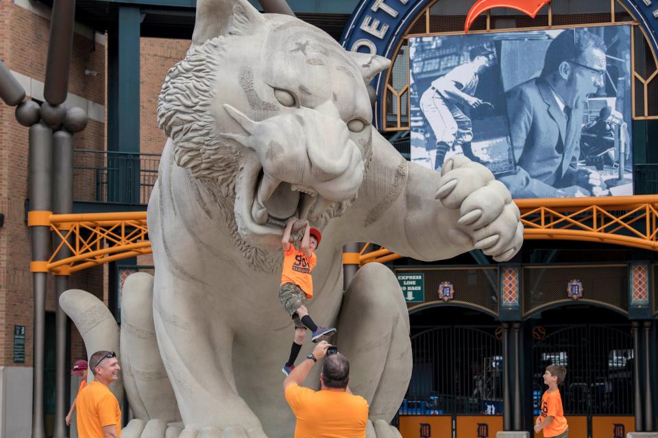 A young boy hangs onto the tooth of a tiger statue in front of Comerica Park before a game between the Dodgers and Tigers on Aug 19, 2017.