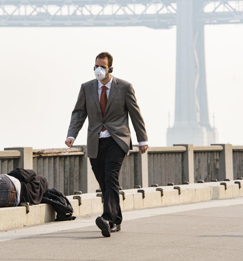 A man wears a mask while another person sleeps on the ground as smoke from the Camp Fire fills the air in San Francisco on Nov. 15, 2018. (Photo: Bloomberg via Getty Images)