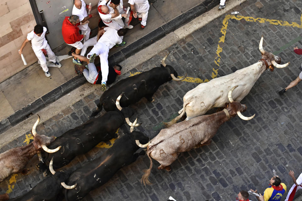 Runners fall as people run through the street with fighting bulls at the San Fermin Festival in Pamplona, northern Spain, Friday, July 8, 2022. Revellers from around the world flock to the city every year for nine days of uninterrupted partying in Pamplona's famed running of the bulls festival which was suspended for the past two years because of the coronavirus pandemic. (AP Photo/Alvaro Barrientos)