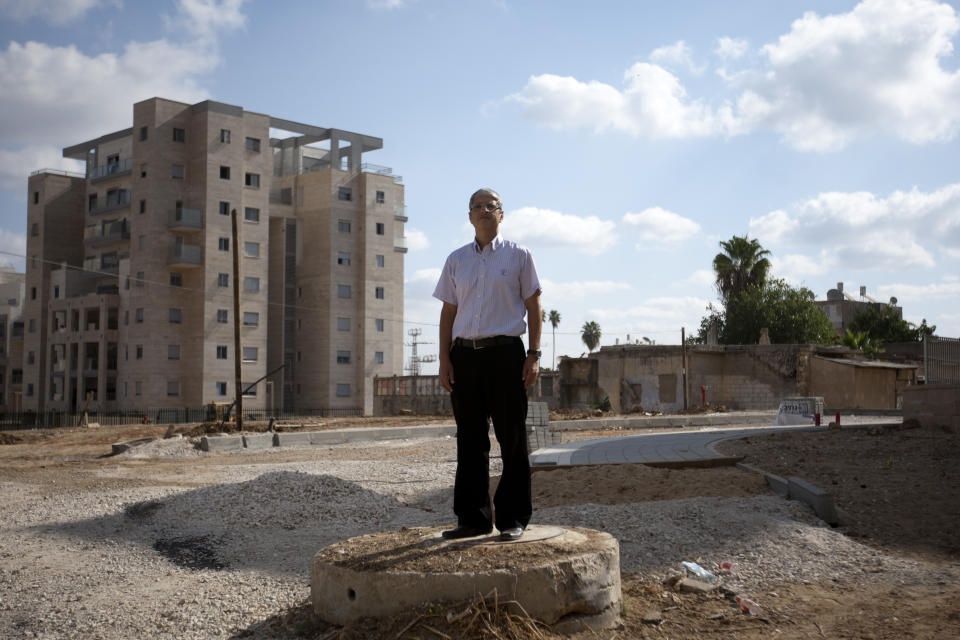 In this photo taken on Thursday, Sept. 20, 2012, Israeli Jewish activist Aharon Attias poses for a photograph in front of new housing project for religious Jews in Israel's mixed Arab-Jewish town of Lod, central Israel. Religious Jews who are the bedrock of the settlement movement have marked Israel's mixed Arab-Jewish cities as the new front to "reclaim," pushing into Arab neighborhoods to cement the Jewish presence there. The migration of several thousand devout Jews to rundown areas of Jaffa, Lod, Ramle and Acco has had a divisive effect far outweighing their absolute numbers, with Jews celebrating _ and Arab activists eyeing with mistrust and resentment _ the construction of Jewish seminaries and housing developments marketed exclusively to Jews. (AP Photo/Ariel Schalit)