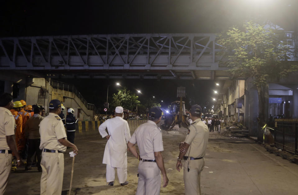 Policemen look at a pedestrian bridge after a part of it collapsed in Mumbai, India, Thursday, March 14, 2019. A pedestrian bridge connecting a train station with a road collapsed in Mumbai on Thursday, killing at least five people and injuring more than 30, police said. (AP Photo/Rajanish Kakade)