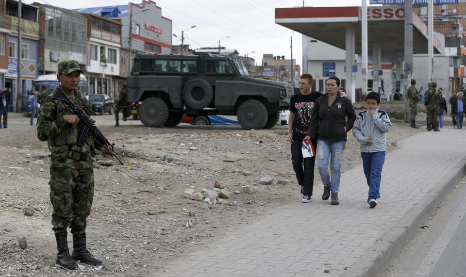 Peatones caminan por una calle vigilada por soldados en el distrito de Soacha, en el sur de Bogotá, Colombia, el viernes 30 de agosto de 2013. Colombia es considerado uno de los países más peligrosos del mundo para los viajeros extranjeros. (Foto AP/Ricardo Mazalán)