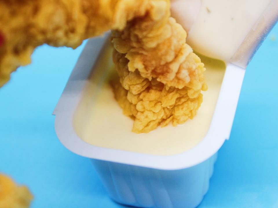 popeyes chicken tender dipped in ranch sauce on blue background