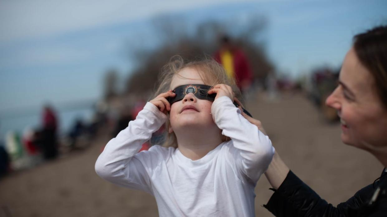 A young girl wearing a pair of eclipse glasses looks to the sky at Point Pelee National Park ahead of the total solar eclipse on Monday, April 8, 2024.  (Dax Melmer/CBC - image credit)