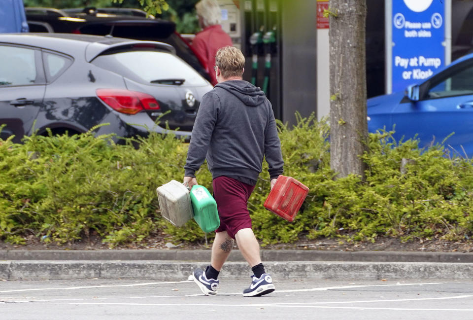 A man carries containers to a petrol station in Bracknell, England, Saturday Sept. 25, 2021. The haulage industry says the U.K. is short tens of thousands of truckers, due to a perfect storm of factors including the coronavirus pandemic, an aging workforce and an exodus of European Union workers following Britain’s departure from the bloc. BP and Esso shut a handful of their gas stations this week, and motorists have formed long lines as they try to fill up in case of further disruption. (Steve Parsons/PA via AP)