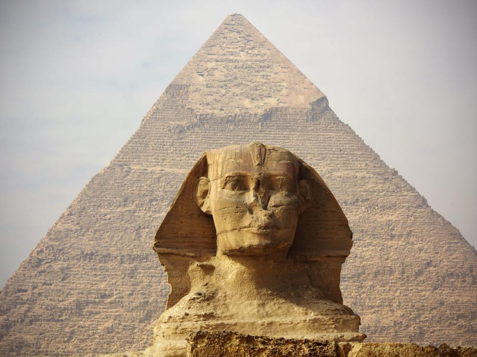 The sphinx is shown in fron of the pyramid which towers over it.