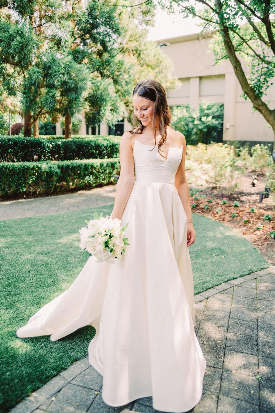 A bride poses in her wedding dress on a lawn.