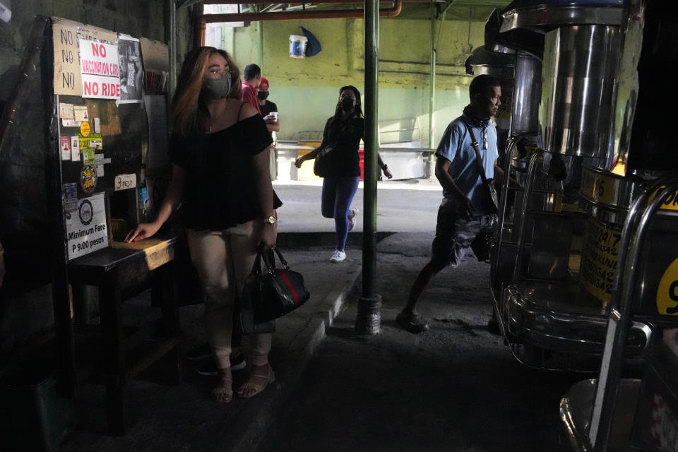 A woman stands beside a sign to remind passengers to show their vaccination card before riding at a jeepney terminal in Quezon city, Philippines on Monday, Jan. 17, 2022. People who are not fully vaccinated against COVID-19 were banned from riding public transport in the Philippine capital region Monday in a desperate move that has sparked protests from labor and human rights groups. (AP Photo/Aaron Favila)