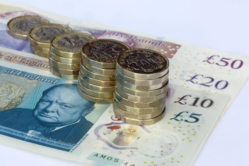 Five stacks of one pound coins arranged in increasing height on British pound notes, £5, £10, £20 and £50, on a white background providing copy space.