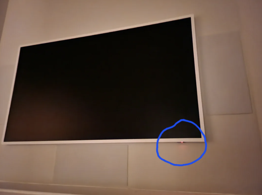 A black-framed screen mounted on a wall with a small, red dot circled in blue near the bottom right corner