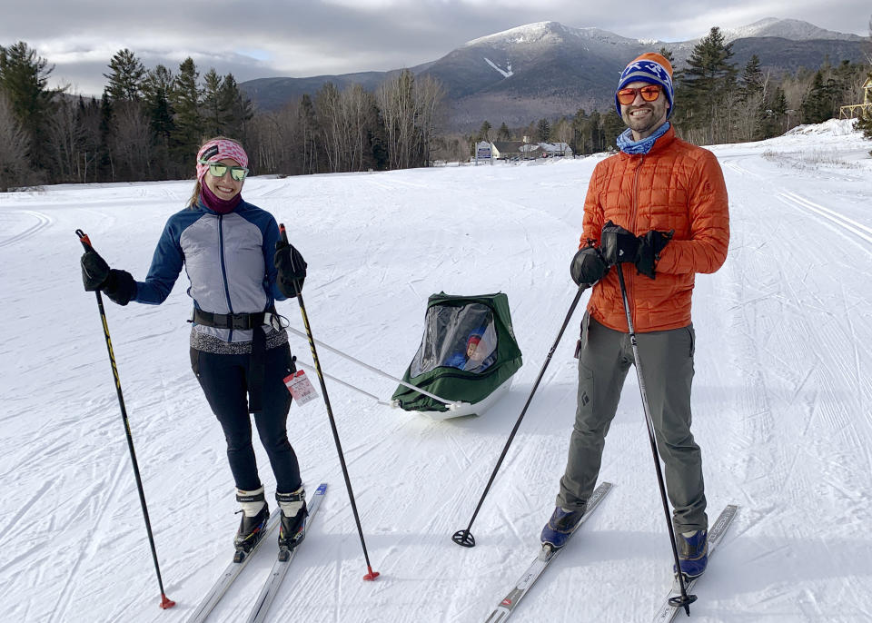 In this photo provided by Nancy Mazonson, Leah Ofsevit, left, and her husband, Jeremy Garczynski, pull their son Lewis Garczynski, in a sled at Waterville Valley Resort, in Waterville Valley, N.H., in January 2022. The New Hampshire resort is about two hours from their home, in Melrose, Mass. The family has lamented the fact that there has been very little snow this winter in the Boston area for them to go sledding and cross country skiing near their home. (Nancy Mazonson via AP)