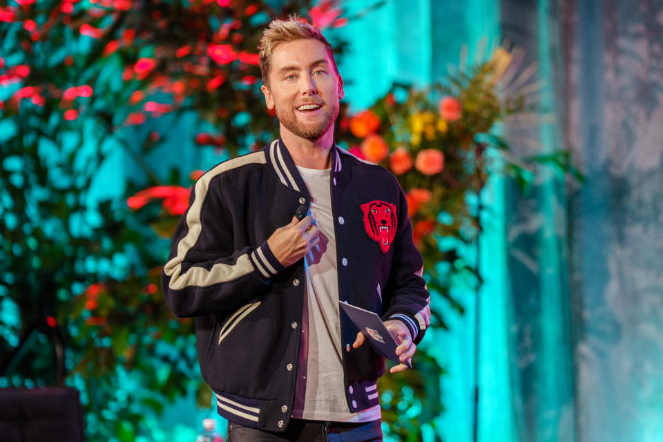 lance bass in a black jackt standing in front of a flowering tree and curtains