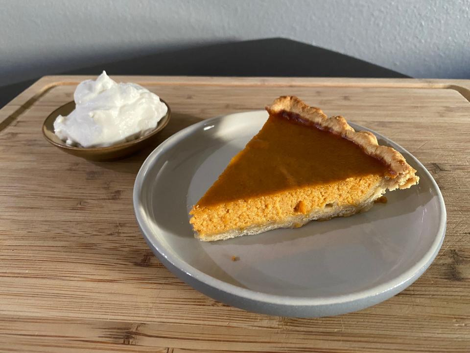slice of ina garten's pumpkin pie with a bowl of homemade  whipped cream next to it