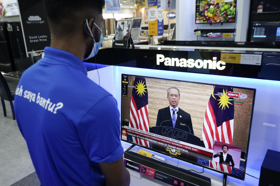 An electronic shop worker wearing a face mask watches a live broadcast of Malaysian Prime Minister Muhyiddin Yassin at a shopping outlet in Kuala Lumpur, Malaysia, Tuesday, Jan. 12, 2021. Malaysia's king Tuesday approved a coronavirus emergency that will prorogue parliament and halt any bids to seek a general election in a political reprieve for embattled Muhyiddin. (AP Photo/Vincent Thian)