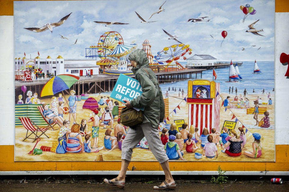 FILE - A woman carries electoral leaflets for Nigel Farage's Reform UK party in Clacton-on-Sea, England, Tuesday, July 2, 2024. United Kingdom voters will cast ballots in a national election Thursday, passing judgment on Sunak’s 20 months in office, and on the four Conservative prime ministers before him. (AP Photo/Vadim Ghirda, File)