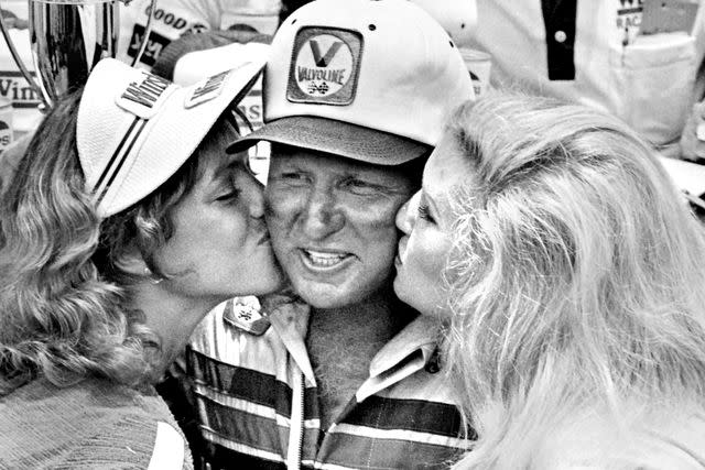 <p>Robert Alexander/Getty</p> NASCAR driver Cale Yarborough is kissed by young female race sponsor representatives in Victory Lane in 1981.