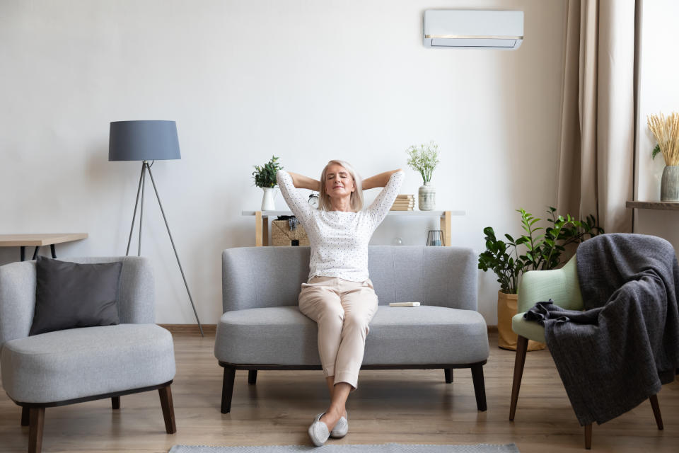 Relaxed satisfied older woman sitting leaning back on couch in air conditioner room, happy peaceful mature female with hands behind head resting on sofa at home, enjoying fresh air, breathing