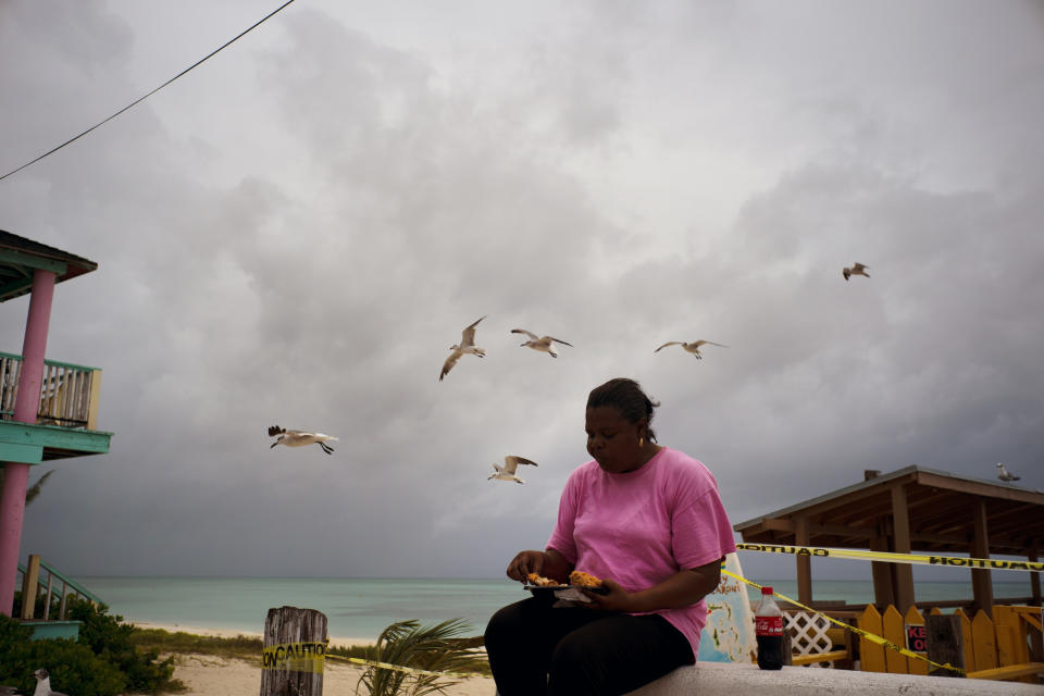 Seagulls fly near a woman feeding them chicken and french fries as dark clouds gather and Hurricane Dorian approaches, on Taino beach in Freeport, Grand Bahama, Bahamas, Sunday Sept. 1, 2019. (AP Photo/Ramon Espinosa)