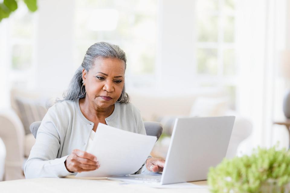 A person at a laptop holding a document.