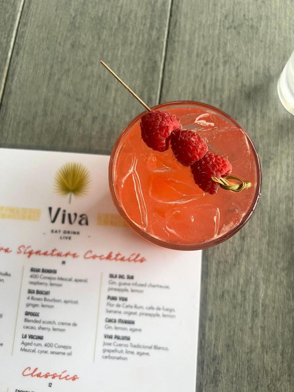 pink cocktail garnished with raspberries sitting on a table with menu