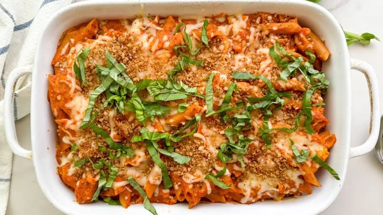 Top-down view of a baking dish of penne topped with herbs 
