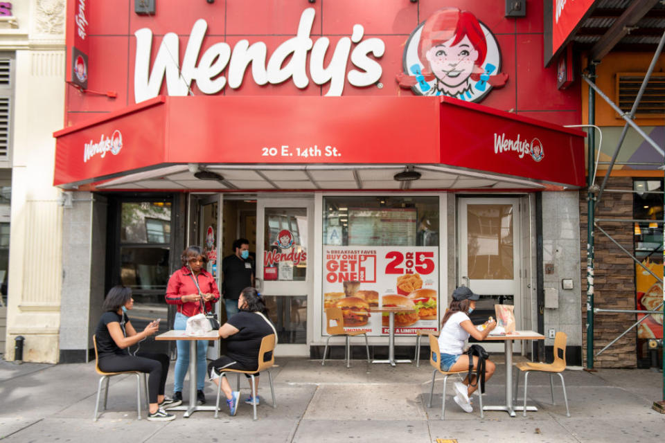 People dining at outdoor tables in front of a Wendy's restaurant