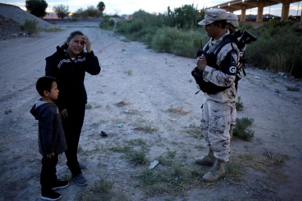 Guatemalan migrant Ledy Pérez reacts while holding hands with her son Anthony while asking to members of the Mexican National Guard to let them cross into the US after traveling 1,500 miles from Guatemala