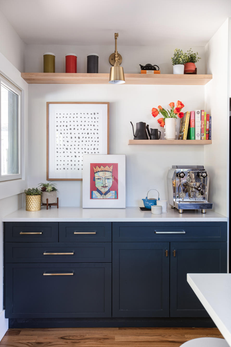 Kitchen nook with dark blue Shaker cabinets, white worktop, oak shelving and a brass wall light