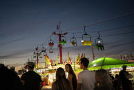 People walk between illuminated booths at the Mississippi State Fair on Wednesday, Oct. 7, 2020, in Jackson, Miss. At the fair, which is held every year in October and attracts people from across the racial spectrum, the vast majority of Black people are wearing masks. Most white people do not. (AP Photo/Wong Maye-E)