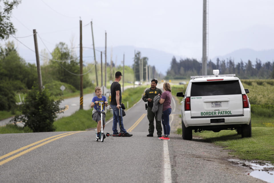 In this photo taken May 17, 2020, a Border Patrol officer in the U.S. talks with nearby residents on E. Boundary Rd., paralleling 0 Ave. behind them in Canada, near Lynden, Wash. With the border closed to nonessential travel amid the global pandemic, families and couples across the continent have found themselves cut off from loved ones on the other side. (AP Photo/Elaine Thompson)