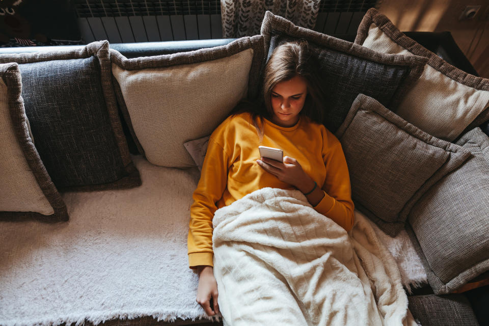 Young woman lying on sofa at living room and using cell phone at home