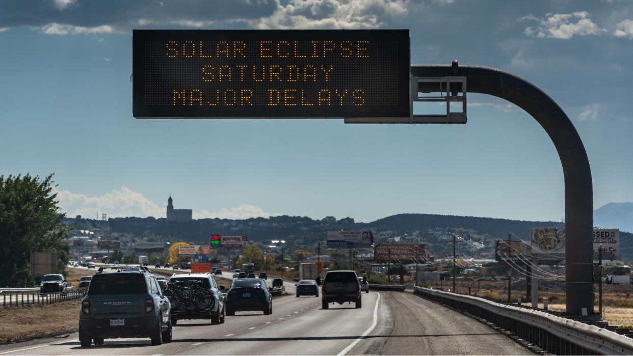  Cars lined up on a highway under a sign reading "solar eclipse saturday major delays". 