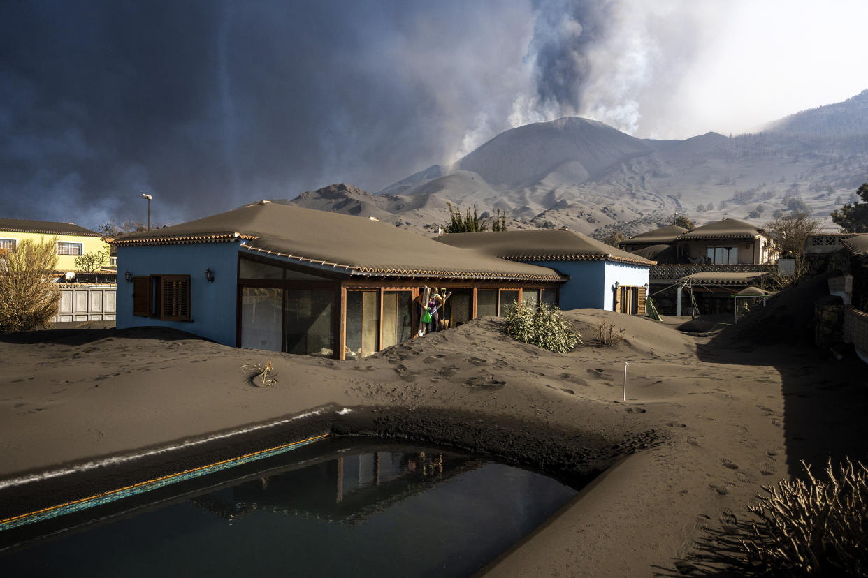 Cristina Vera leaves her house covered with ash from volcano eruptions, after collecting her last belonging at the Canary island of La Palma, Spain, Monday, Nov. 1, 2021. A volcano on the Spanish island of La Palma that has been erupting for six weeks has spewed more ash from its main mouth a day after producing its strongest earthquake to date. (AP Photo/Emilio Morenatti)