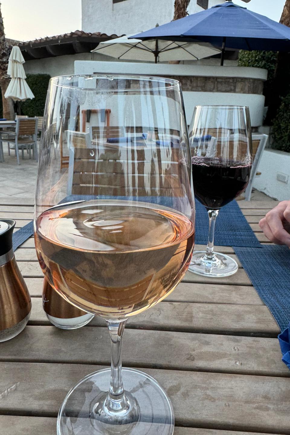 Two glasses of wine, one red and one rosé, on an outdoor table with umbrellas in the background