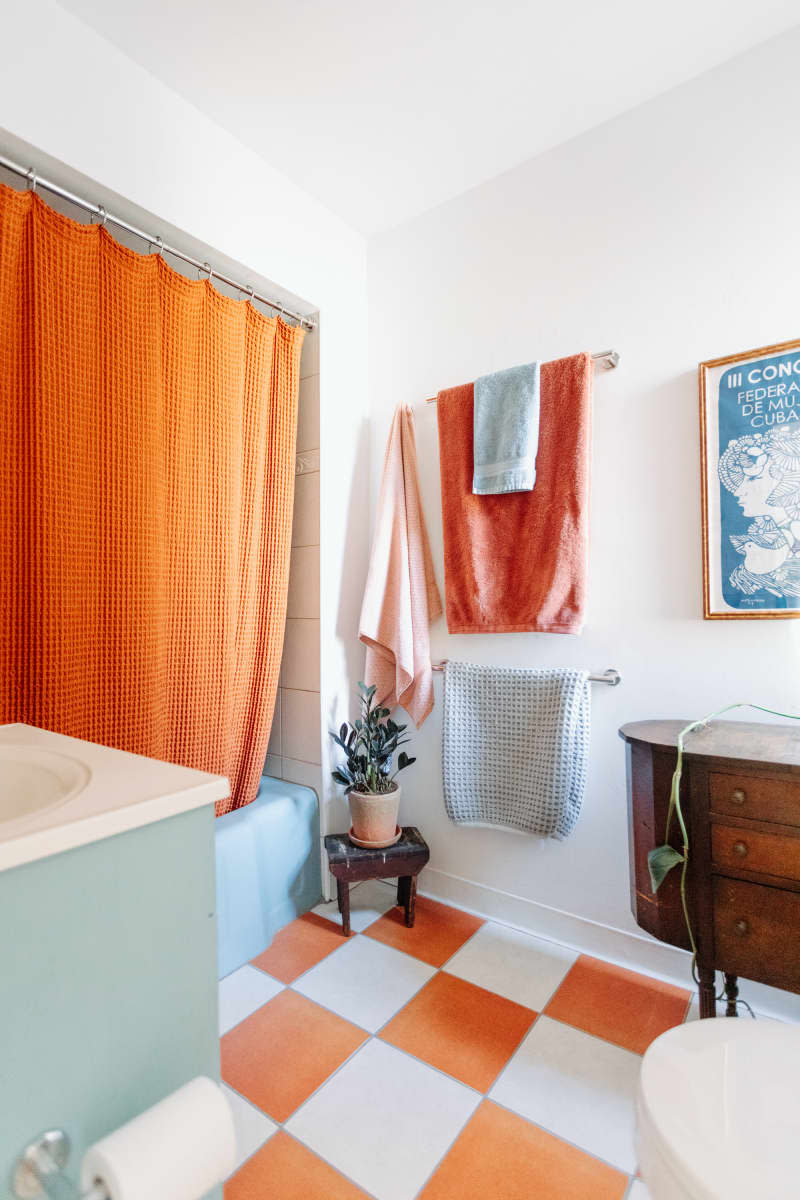 Corner view of white bathroom with orange accents and checkerboard floor.