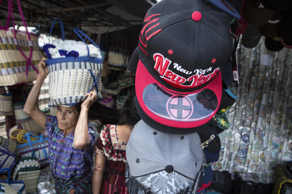 A woman carries a basket on her head as she walks through a store that sells hats with motifs from different cities from the United States, in San Martin Jilotepeque, Guatemala, Sunday, August 4, 2019. San Martin Jilotepeque, like other towns in Guatemala, depends to a large extent on remittances, the money sent home by migrants living in the United States. (AP Photo/ Oliver de Ros)