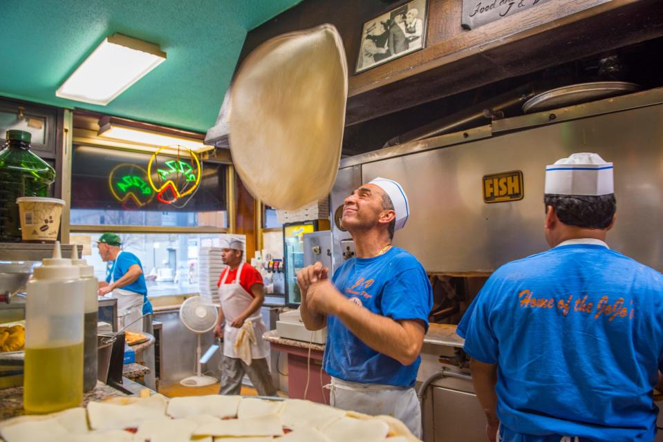 A cook flipping pizza dough in a kitchen.