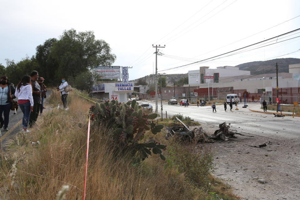 Locals walk past a burned-out car outside the Tula General Hospital, after a gang rammed several vehicles into a prison and escaped with nine inmates, in Tula, Mexico, Wednesday, Dec. 1, 2021. Local media reported that the burned-out cars found in the city after the attack were car bombs. Authorities said they were investigating how the vehicles caught fire. (AP Photo/Ginnette Riquelme)