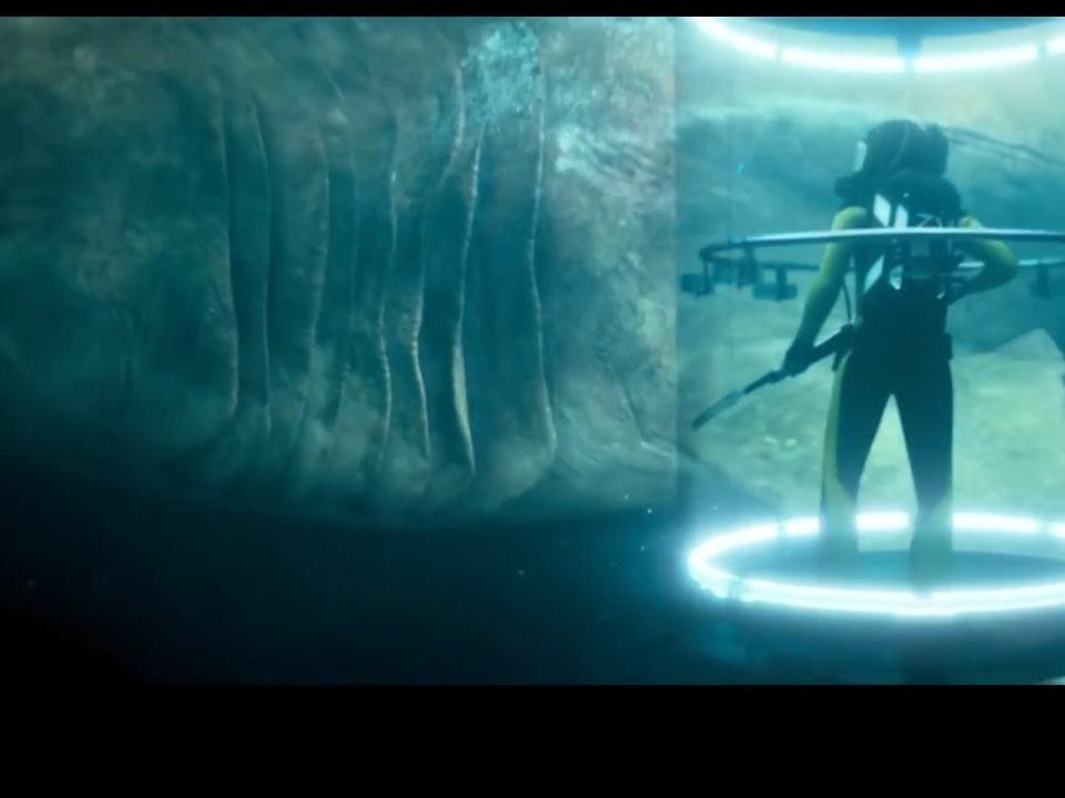 A still from "The Meg" shows the huge shark swimming behind a shark cage containing a human holding a spear gun. Eight gills, which are as big as the human, are clearly visible.