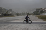A man rides his bicycle past fields covered with volcanic ash a day after the La Soufriere volcano erupted, in Kingstown, on the eastern Caribbean island of St. Vincent, Saturday, April 10, 2021. (AP Photo/Lucanus Ollivierre)