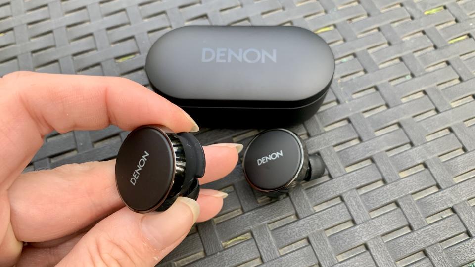 Denon PerL Pro earbud held in a hand, with the case in the background on a black table