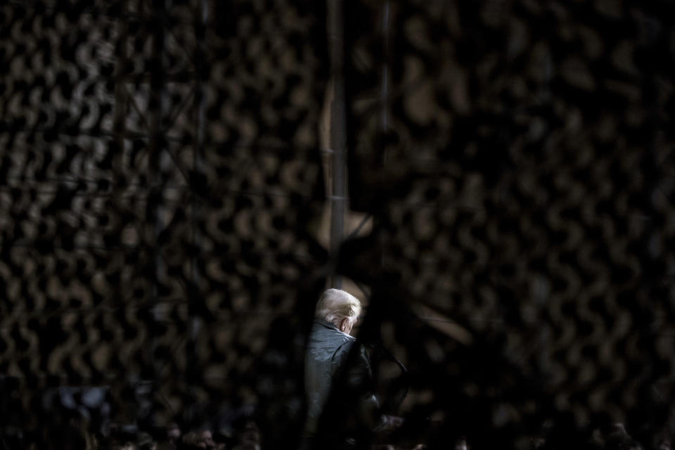 President Donald Trump is seen through camouflage netting as he speaks at a hanger rally at Al Asad Air Base, Iraq, Wednesday, Dec. 26, 2018. In a surprise trip to Iraq, President Donald Trump on Wednesday defended his decision to withdraw U.S. forces from Syria where they have been helping battle Islamic State militants. (AP Photo/Andrew Harnik)