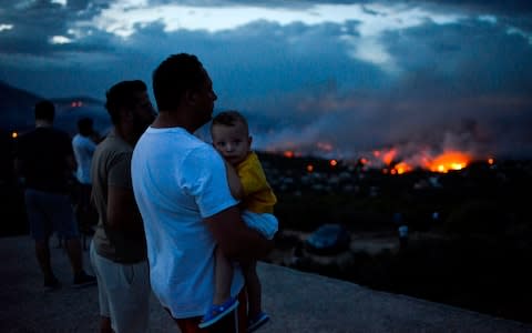 A man holds his son as a wildfire burns in the town of Rafina, near Athens - Credit: AFP