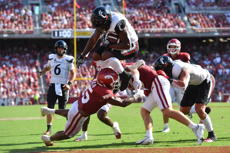 Cincinnati running back Corey Kiner (2) leaps over Arkansas defensive back Simeon Blair (15) to score a touchdown during the second half of an NCAA college football game Saturday, Sept. 3, 2022, in Fayetteville, Ark. (AP Photo/Michael Woods)