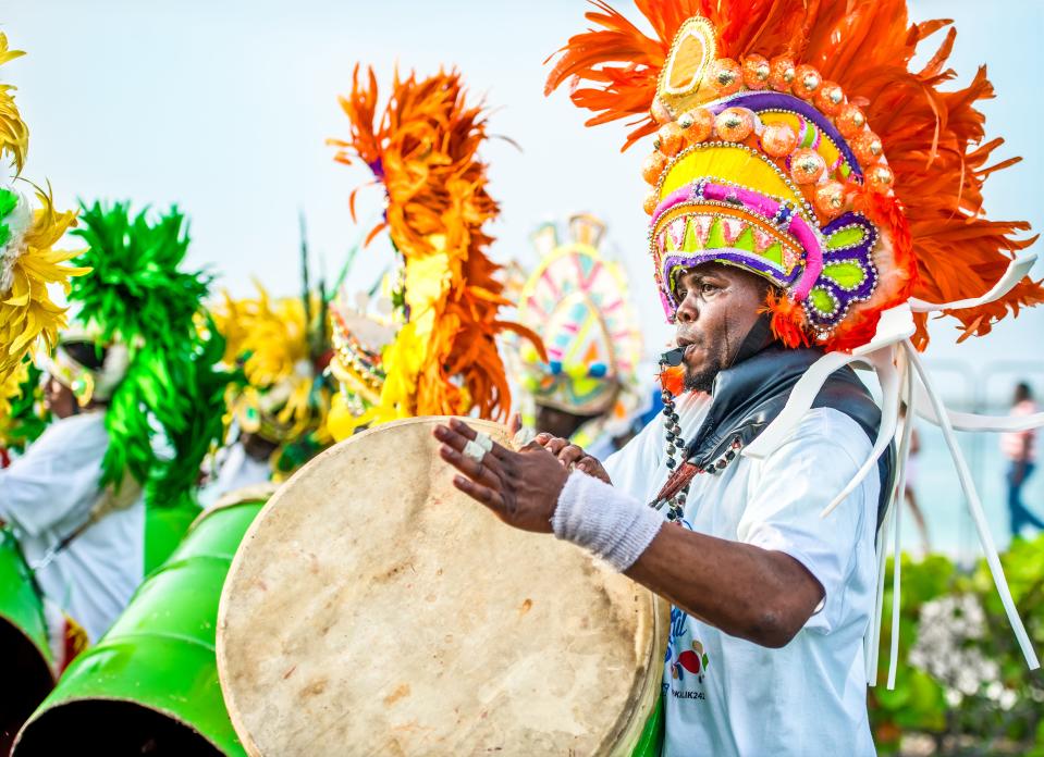 A Junkanoo drummer wearing a cardboard decorated colorful headpiece plays a goatskin drum during the parade.