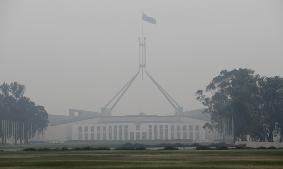 The Australian flag flies above Parliament House as smoke shrouds the Australian capital of Canberra, Australia, Wednesday, Jan. 1, 2020. Australia deployed military ships and aircraft to help communities ravaged by apocalyptic wildfires that destroyed homes and sent thousands of residents and holidaymakers fleeing to the shoreline. (AP Photo/Mark Baker)