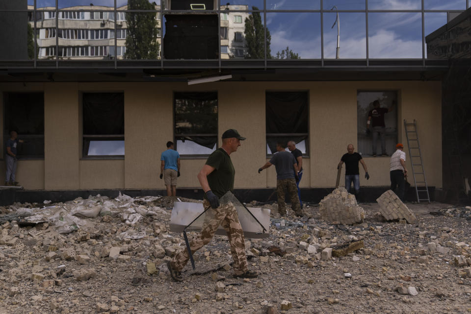 Varias personas limpian los escombros en el exterior de un edifico gubernamental dañado en Kiev, Ucrania, el 2 de agosto de 2023, luego de ataques rusos con drones. (AP Foto/Jae C. Hong)